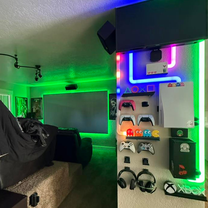 Tobin’s afterHIDEit home theater and game room featuring a PS5, Xbox Series X, Nintendo Switch, controllers, and headsets mounted on an LED gaming wall with decorative cable covers.