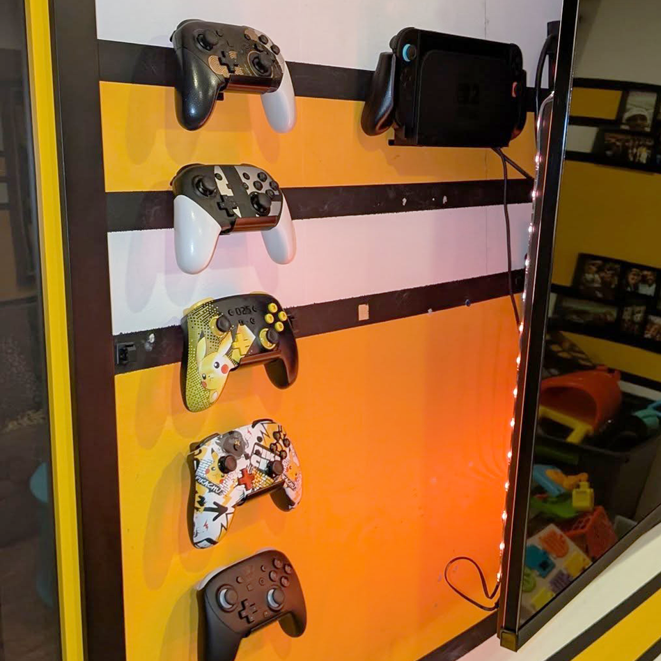 Will’s gaming room wall with a colorful controller collection mounted on HIDEit Controller Mounts and accented with LED lighting for organized accessory display.