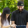 Woman in all black embroidered New Era hat with HIDEit logo. Man holding iPad with the new HIDEit Mounts snapback hat.