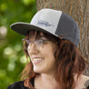 Woman in a gray HIDEit Mounts hat with an embroidered logo in the bottom corner of the hat.